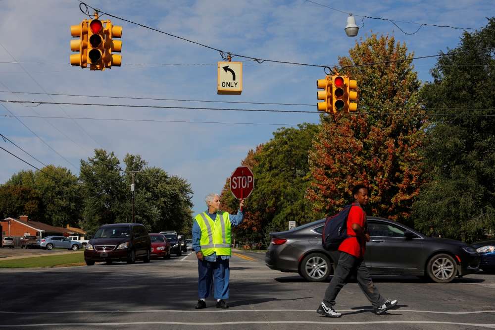 Crossing guard Barbara Elliott helps a student across an intersection in Precinct 7, where the vote was split 876/876 between Donald Trump and Hillary Clinton in 2016, in Saginaw Township, Michigan, in this Oct. 10, 2019 file photo. — Reuters