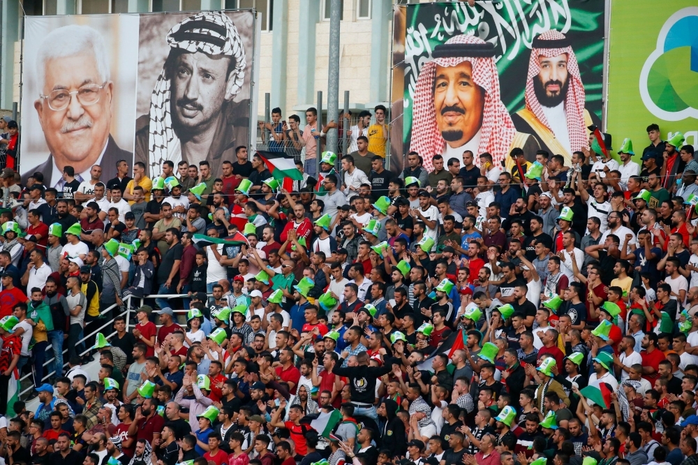 Football fans stand beneath a large banner depicting Saudi Arabia's King Salman (C) and his son Crown Prince Mohammed bin Salman (R) as they attend the World Cup 2022 Asian qualifying match between Palestine and Saudi Arabia in the town of Al-Ram, West Bank, on Tuesday. — AFP