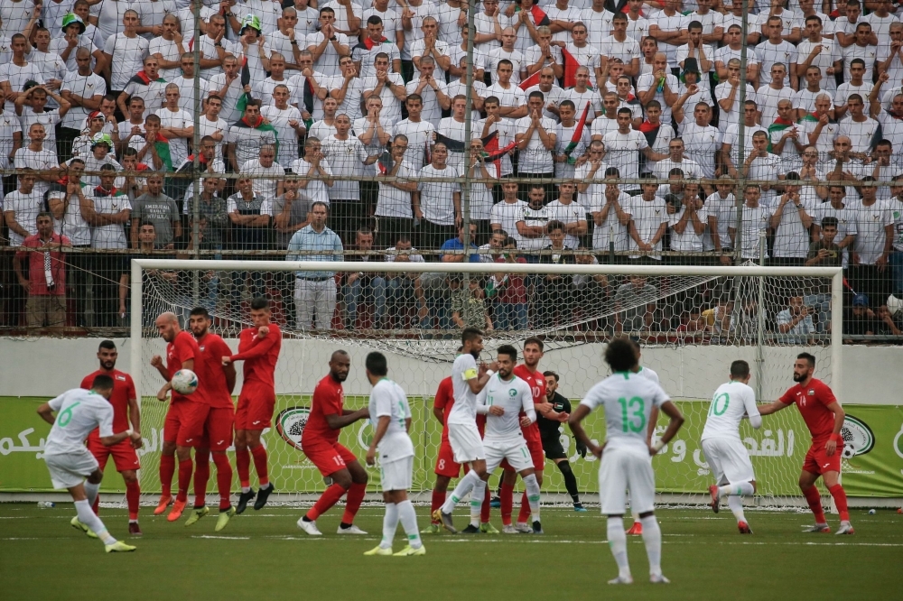 Football fans stand beneath a large banner depicting Saudi Arabia's King Salman (C) and his son Crown Prince Mohammed bin Salman (R) as they attend the World Cup 2022 Asian qualifying match between Palestine and Saudi Arabia in the town of Al-Ram, West Bank, on Tuesday. — AFP