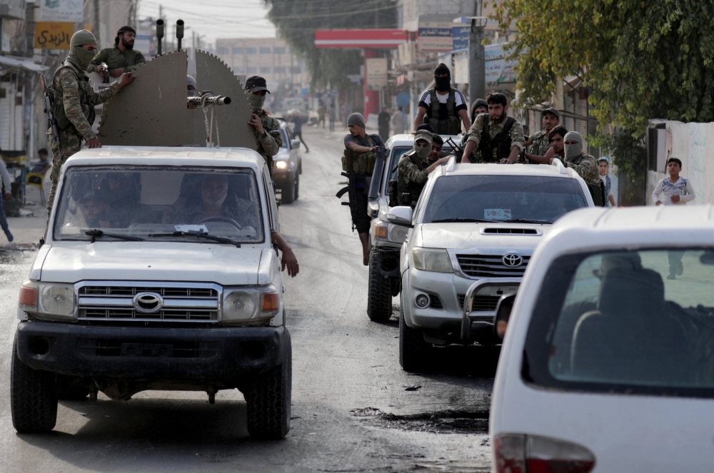 Turkey-backed Syrian rebel fighters ride at the back of a truck mounted with a weapon in the border town of Tal Abyad, Syria, on Tuesday. — Reuters