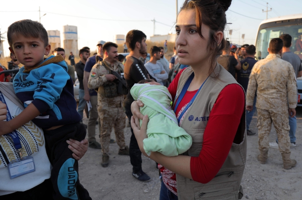 People holding children disembark from a minibus transporting Syrians who have been recently-turned refugees by the Turkish military operation in northeastern Syria upon arriving at the Bardarash camp, near the Kurdish city of Dohuk, in Iraq's autonomous Kurdish region, on Wednesday. — AFP