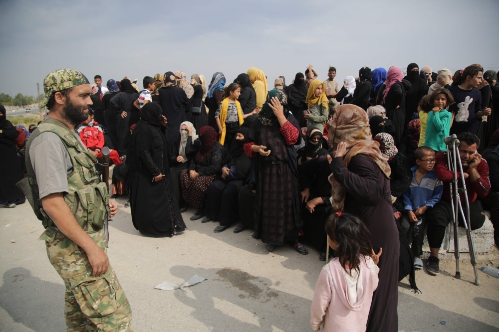 A member of the Turkey-backd forces looks at displaced Syrians waiting to receive aid provided by the Turkish Red Crescent, in the Syrian border town of Tal Abyad which was seized last week. Turkish and Kurdish leaders traded accusations of violating a US-brokered truce in northeastern Syria, which aimed to halt a Turkish-led offensive on Kurdish forces that has killed dozens of civilians and prompted hundreds of thousands to flee their homes, in the latest humanitarian crisis of Syria's eight-year civil war. — AFP