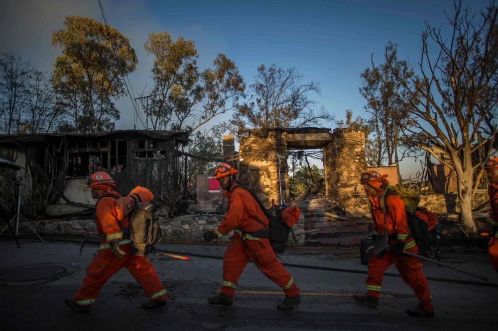Inmate firefighters walk past a burnt home on Tigertail road during the Getty Fire in Brentwood, California, on Monday. — AFP 