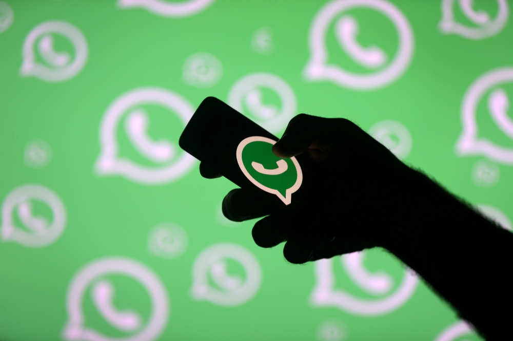 A man poses with a smartphone in front of displayed Whatsapp logo in this illustration Sept. 14, 2017. — Reuters
