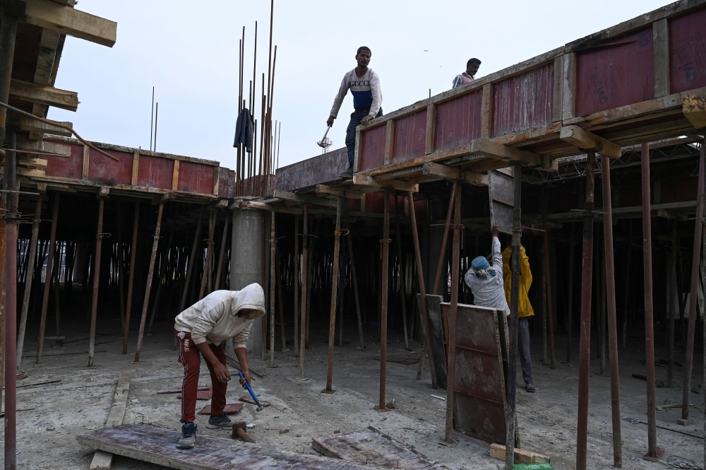 Migrant laborers work at a building construction site in Srinagar. — AFP