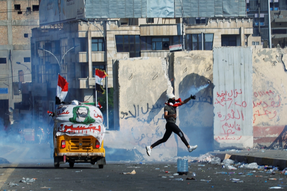 A demonstrator throws away a tear gas canister during an anti-government protests in Baghdad on Friday. — Reuters