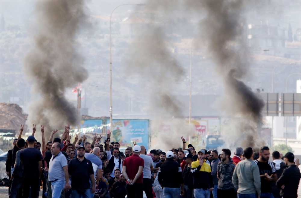  Lebanese protesters gather next to burning tires to block the southern entrance of the capital of north Lebanon Tripoli, as anti-government demonstrations continued on Tuesday across the country. -AFP