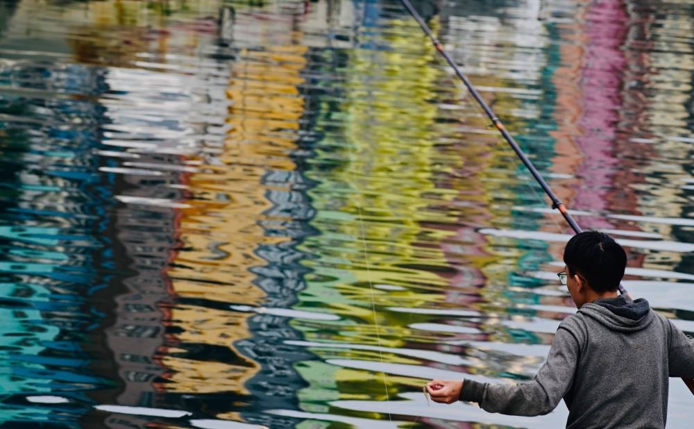 A man fishing at the Zhangbin Fishing Port as the water reflects the color painted houses in Keelung, northern Taiwan. — AFP 