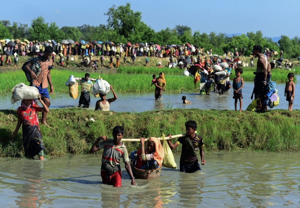 Rohingya refugees carry a woman over a shallow canal after crossing the Naf River as they flee violence in Myanmar to reach Bangladesh in Palongkhali near Ukhia in this Oct. 16, 2017 file photo. — AFP