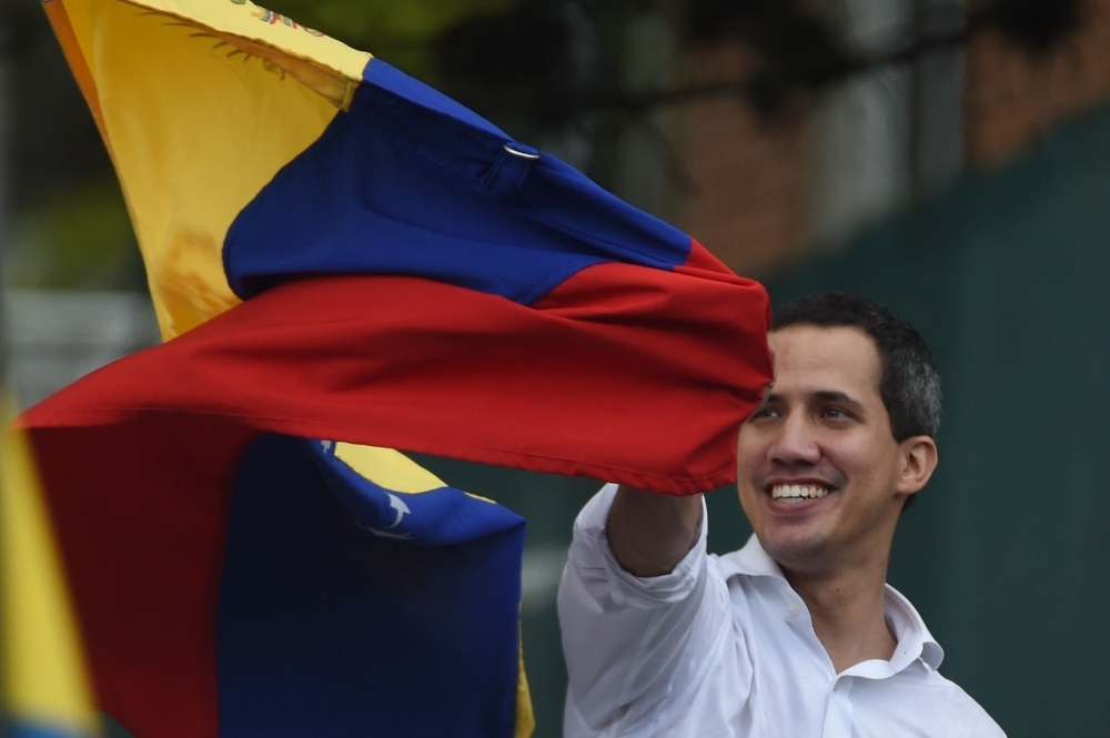Venezuelan opposition leader and self-proclaimed acting president Juan Guaido displays a national flag during a gathering in front of the Bolivian embassy in Caracas on Saturday. -AFP