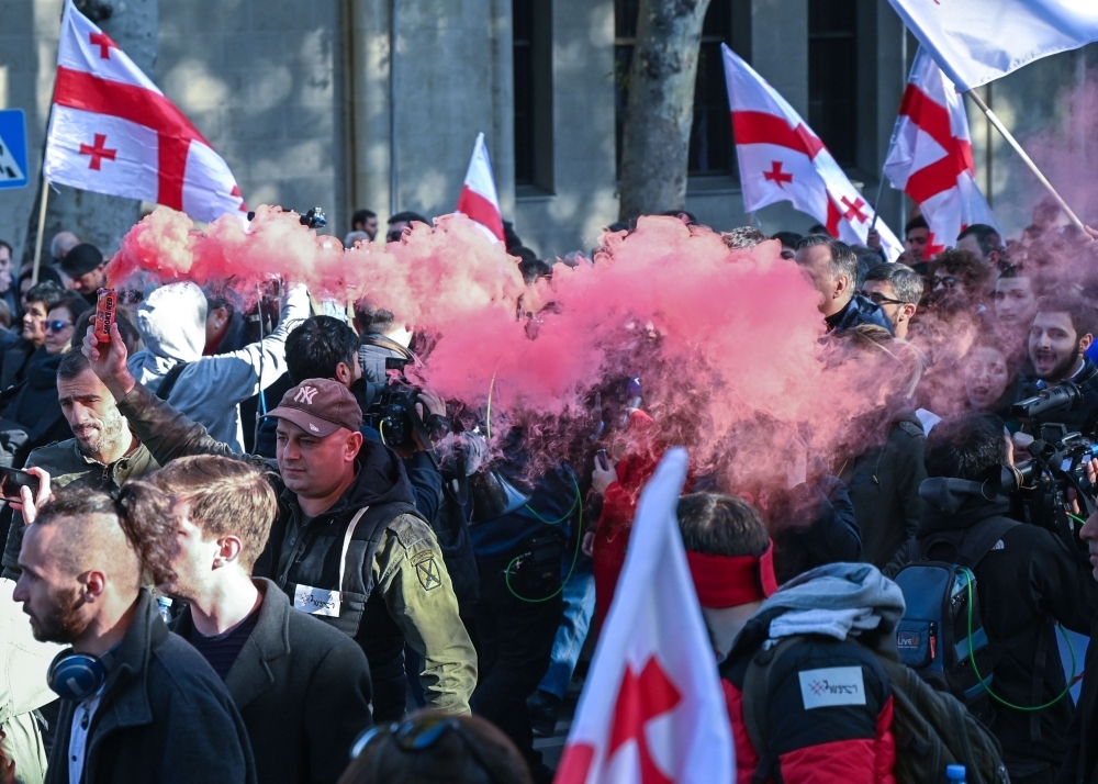 Georgian opposition supporters hold smoke flares and Georgian flags as they protest outside the parliament in central Tbilisi on Sunday. -AFP