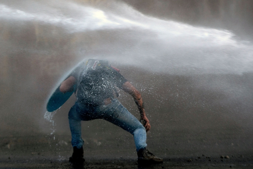  A demonstrator leans to elude the riot police water cannon during a protest against the government in Santiago on Tuesday. -AFP