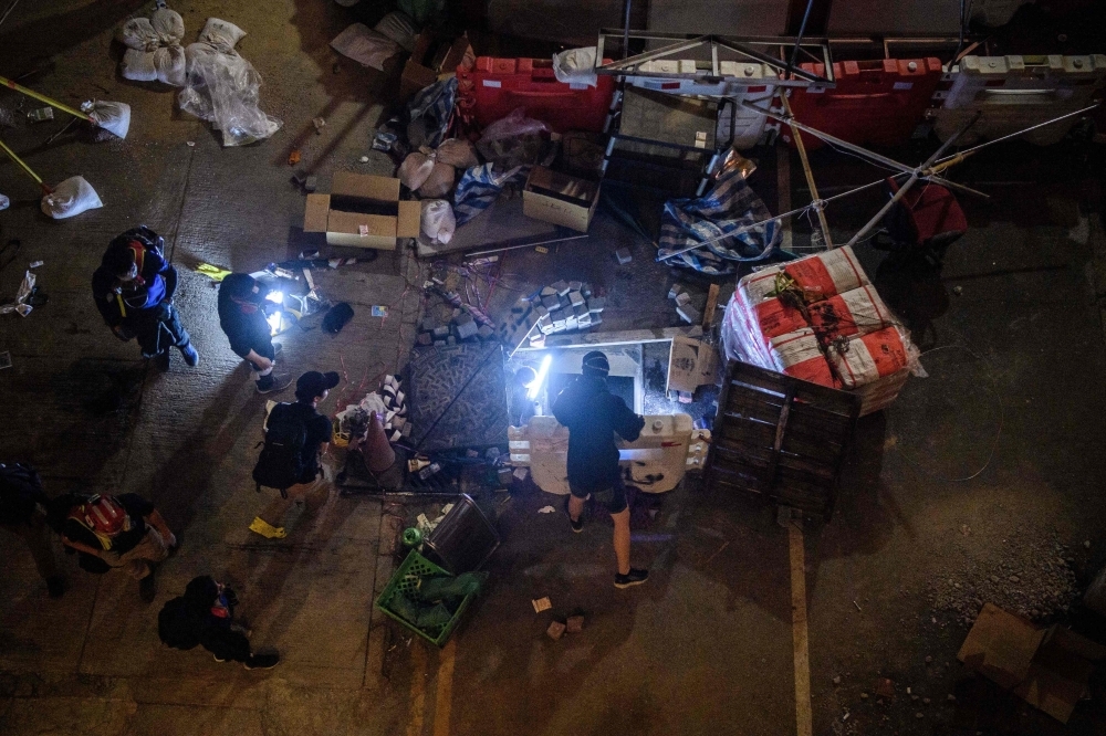 A protester climbs down into a sewer entrance with a guide string, center, as he and others try to find an escape route from the Hong Kong Polytechnic University in the Hung Hom district of Hong Kong, early morning on Tuesday. — AFP
