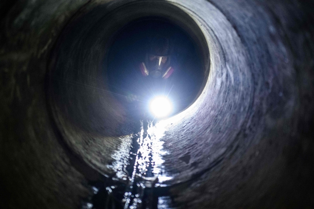 A protester climbs down into a sewer entrance with a guide string, center, as he and others try to find an escape route from the Hong Kong Polytechnic University in the Hung Hom district of Hong Kong, early morning on Tuesday. — AFP