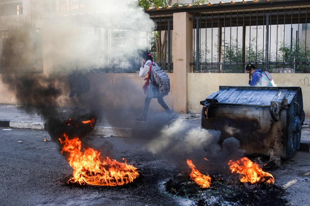 A school girl walks past flaming tires set by anti-government protesters to block roads in the southern city of Sidon in this Nov. 19, 2019 file photo. — AFP
