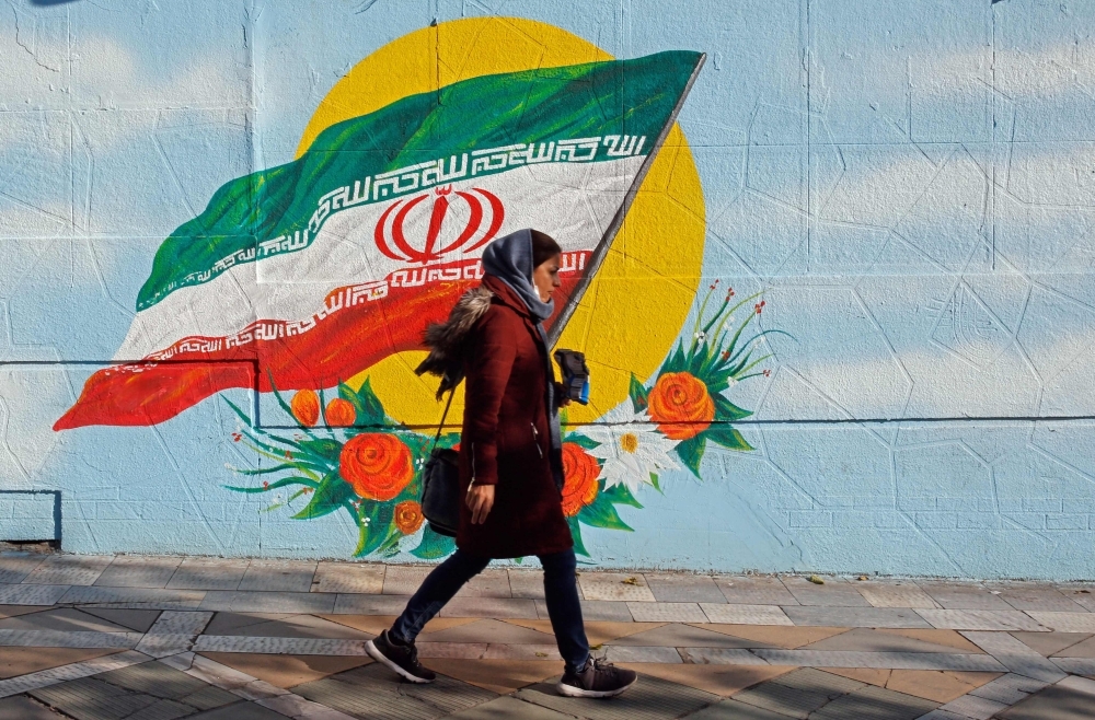 An Iranian woman walks past a mural painting of the Islamic republic's national flag in central Tehran on Thursday. — aFP