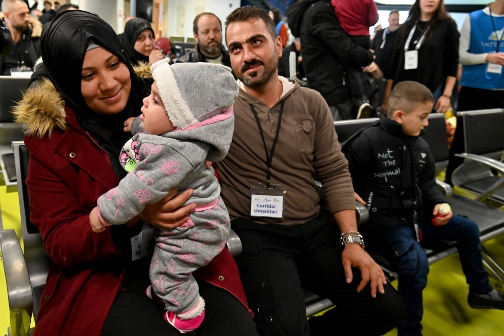 Syrian refugees Ibrahim Bitar, 42, rear right with red jersey, and his sister Iman Bitar, center from behind, react after arriving with other Syrian refugees at Rome's Fiumicino international airport as part of a humanitarian corridor on Wednesday. — AFP