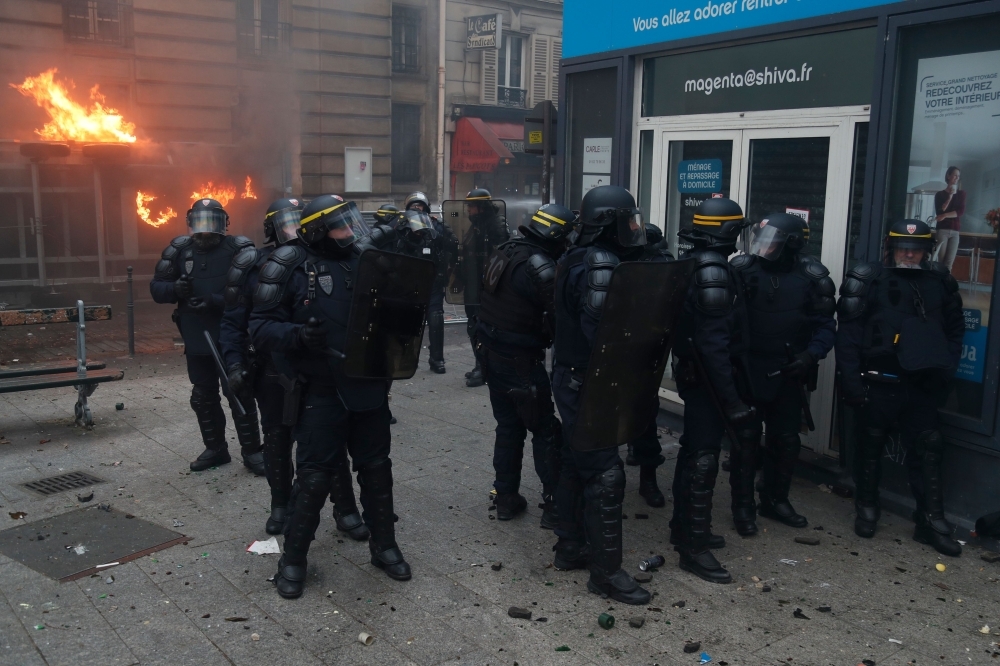 CRS riot police stand as fire is seen in the background during a rally against the pension overhauls, in Paris, on Thursday. — AFP