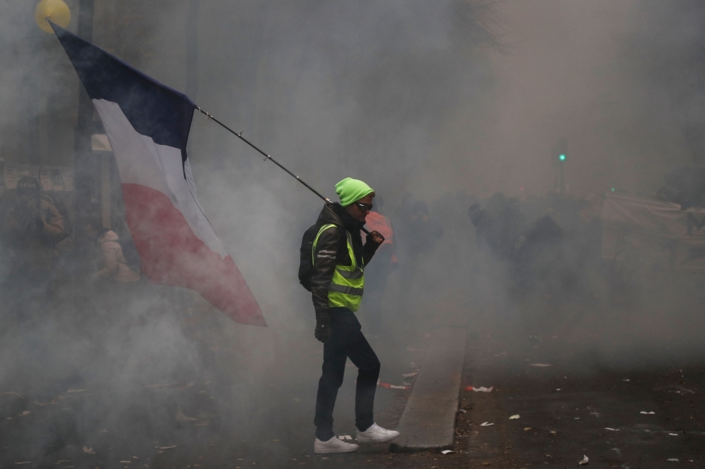 CRS riot police stand as fire is seen in the background during a rally against the pension overhauls, in Paris, on Thursday. — AFP