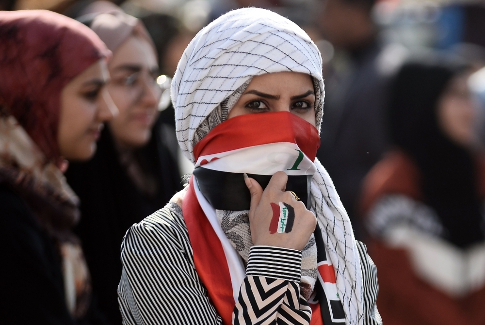 An Iraqi student covers her face with a national flag as she takes part in an anti-government demonstration in the central city of Najaf on Wednesday. — AFP