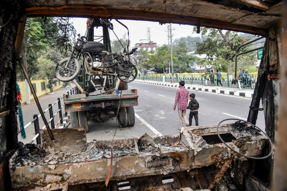 People walk past the wreckage of a vehicle which was set on fire by demonstrators during a protest against the government's Citizenship Amendment Bill (CAB) in Guwahati on Thursday. — AFP