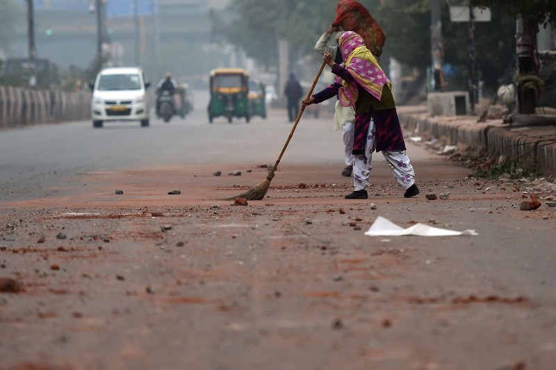 A municipal corporation employee sweeps up stones and parts of bricks left on the road after the previous day's protest against India's new citizenship law in New Delhi on Wednesday. -AFP