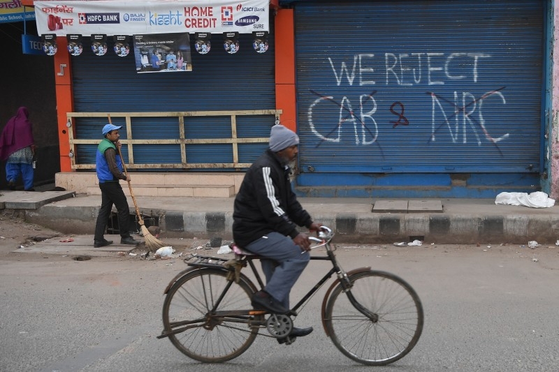 A municipal corporation employee sweeps up stones and parts of bricks left on the road after the previous day's protest against India's new citizenship law in New Delhi on Wednesday. -AFP