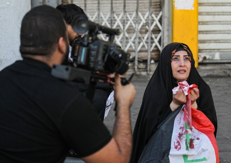 A cameraman films an actress performing a scene as she reacts while holding up a red-stained Iraqi national flag, in Rasheed street in the capital Baghdad, on Wednesday. — AFP