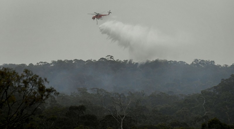 A helicopter dumps water on a bushfire in the outer suburbs of Melbourne, Australia, on Monday. — AFP