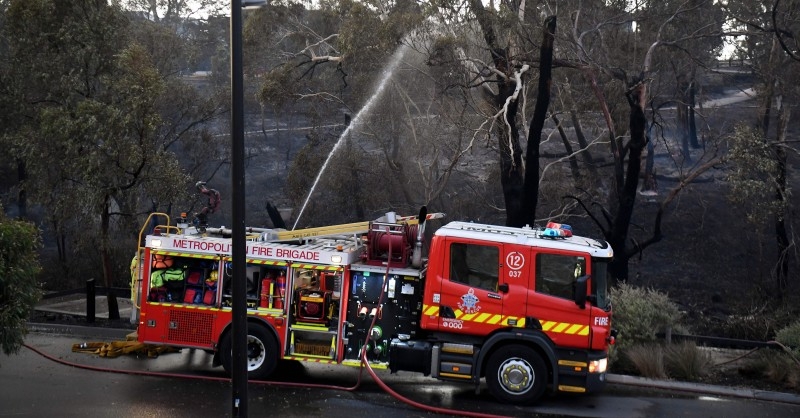 A helicopter dumps water on a bushfire in the outer suburbs of Melbourne, Australia, on Monday. — AFP