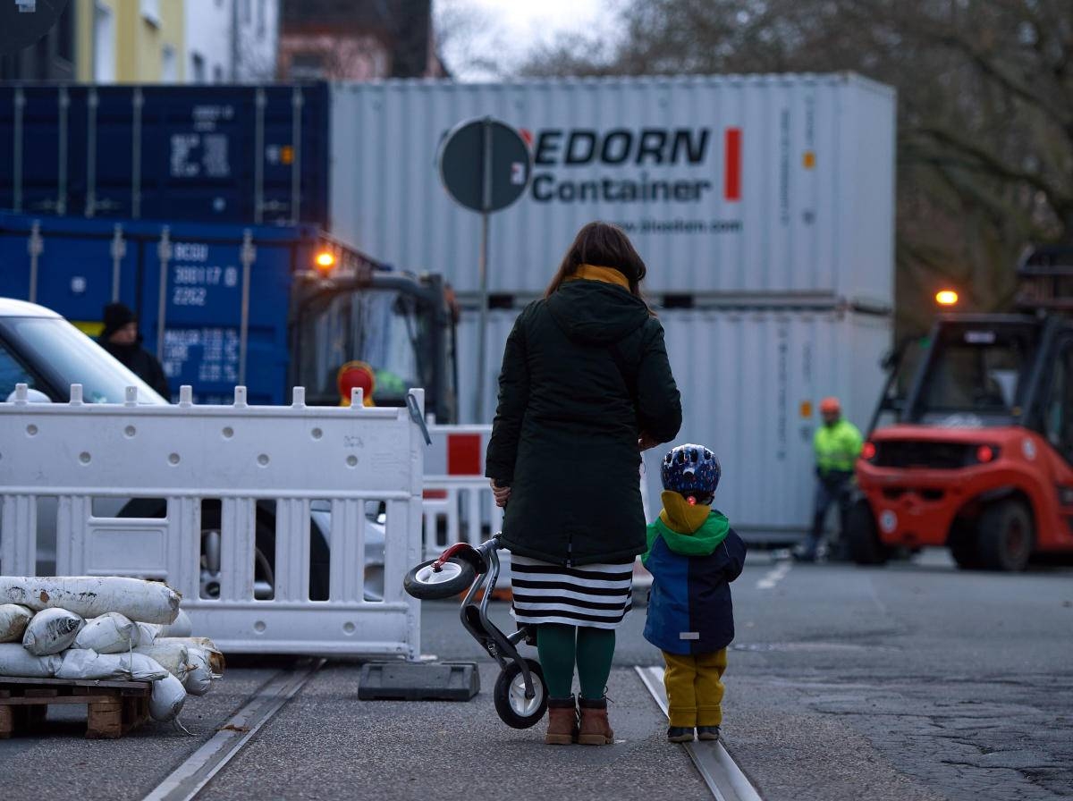A woman and child stand in front of a wall made up of containers erected by workers to protect the houses in a street where World War II bombs were discovered in Dortmund, western Germany. — AFP
