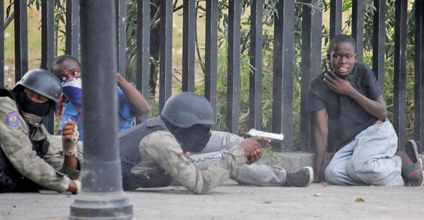 A boy gestures as a man in a Haitian National Police uniform aims a gun during a shooting in Champ de Mars, Port-au-Prince, Haiti, on Sunday. — Courtesy photo