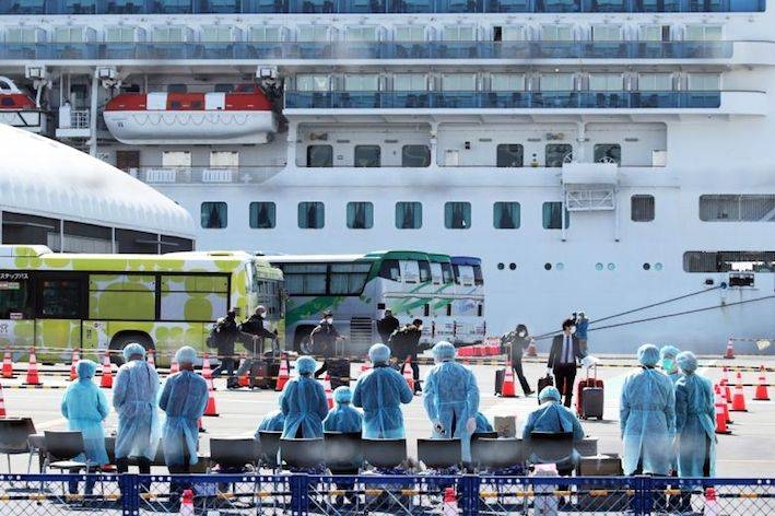 Workers in protective gear prepare to check passengers after they disembark from the Diamond Princess cruise ship, which has been quarantined, at the Daikoku Pier Cruise Terminal in Yokohama, Japan, on Feb. 21, 2020. Crew members began leaving the vessel Thursday for a new quarantine on-shore.