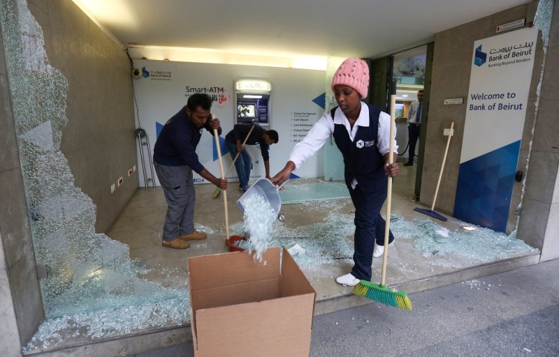 A woman cleans up glass from a broken facade of a bank in Beirut, Lebanon, after anti-government protests.