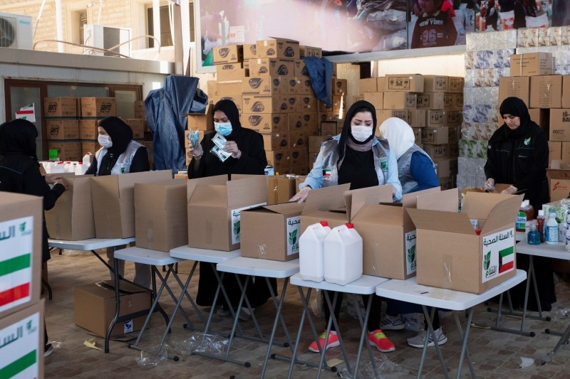 Kuwaiti volunteers wear protective masks as they fill charity boxes with essential household supplies to distribute to the needy. -- File photo