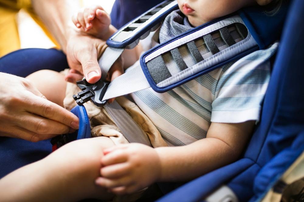 A father fastening seat belt for his son sitting in safety seat in the car.