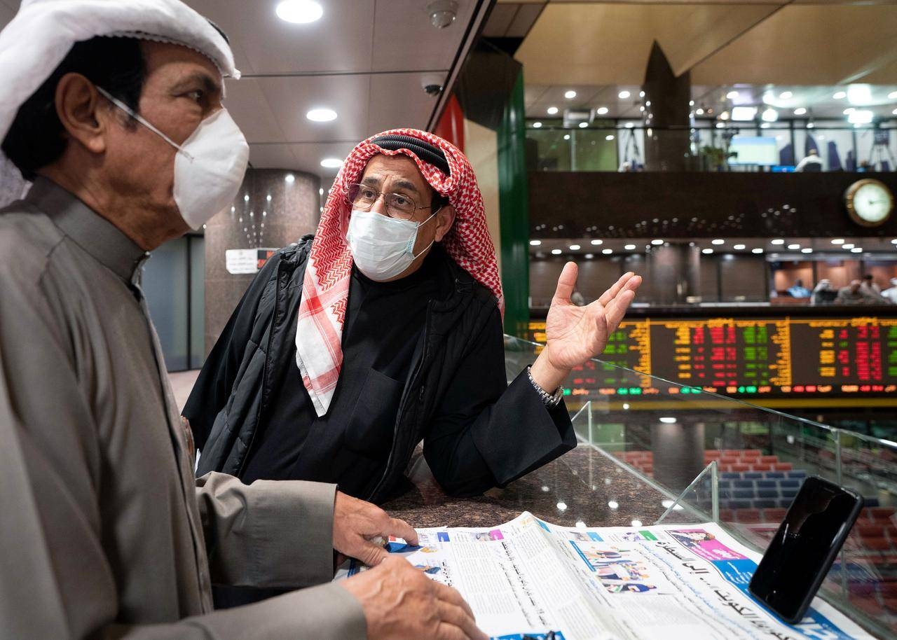 Traders wear protective face masks as they stand on the upper floor since the lower main hall is closed to traders at the Kuwait stock market trading in Kuwait City. -- File photo