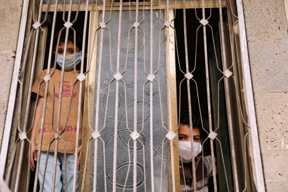 Children wearing protective masks look from behind a window during a 24-hour curfew amid concerns about the spread of the coronavirus disease (COVID-19), in Sanaa. — Courtesy photo