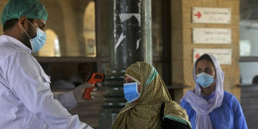 A railway worker checks the body temperature of a woman wearing a protective mask on her arrival at a railway station in Karachi. — Courtesy photo
