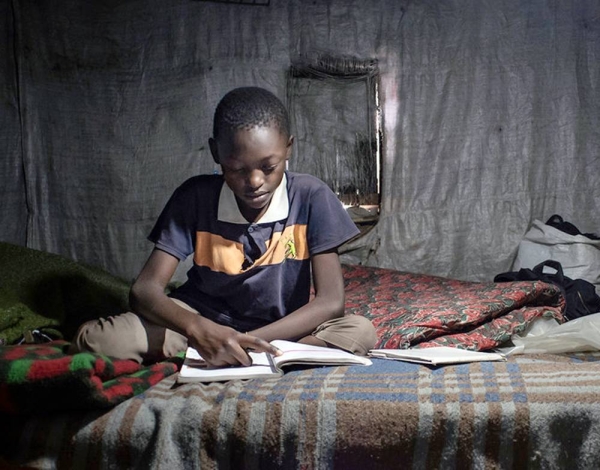 An 11-year-old child studies his Class 6 textbooks and revises the exercises at home in Nairobi, Kenya. He cannot participate in online learning as his family has no mobile phone. — courtesy UNICEF/Everett