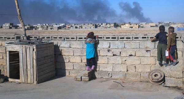 In Iraq, children look over a wall at clouds of smoke from burning oil wells, the result of oil fires set by ISIL. — courtesy UNICEF/Lindsay Mackenzie