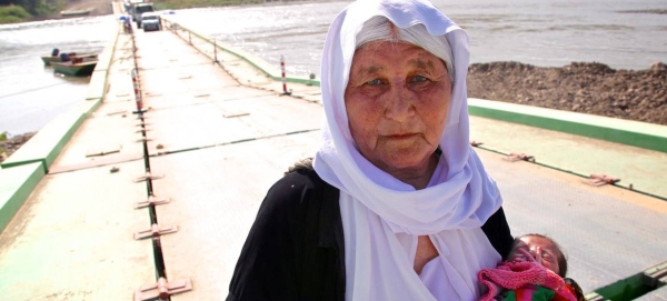 Holding a 13-day-old infant, an elderly Yazidi woman who fled Sinjar Mountain re-enters Iraq from Syria. — UN news