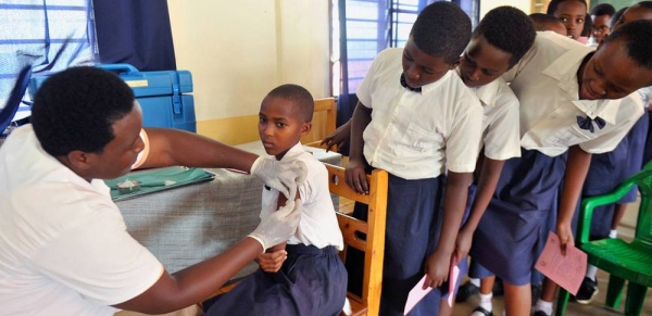A young girl in Rwanda receives her HPV vaccination while her classmates nervously wait their turn. — courtesy UNICEF/Laurent Rusanganwa