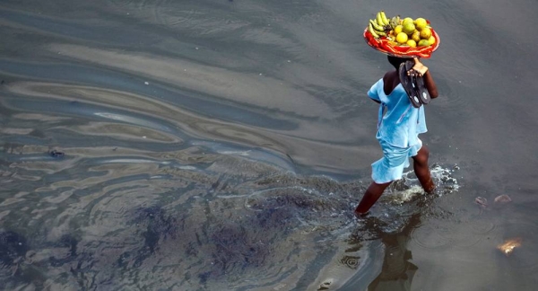 A girl carries a basket of fruits through a flooded street in Cotonou, a large port city in Benin. — courtesy UNICEF/Oliver Asselin