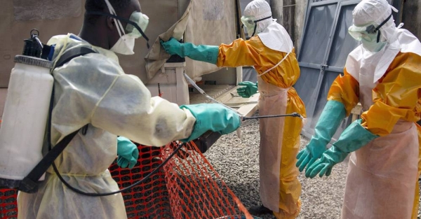 
In this photograph from 2015, an IFRC worker sprays disinfecting chlorine solution on the gloved hands of a fellow worker in Conakry, Guinea. The country was one of the worst-affected in the 2014-2016 West Africa Ebola outbreak. — courtesy UNICEF/UNMEER Martine Perret