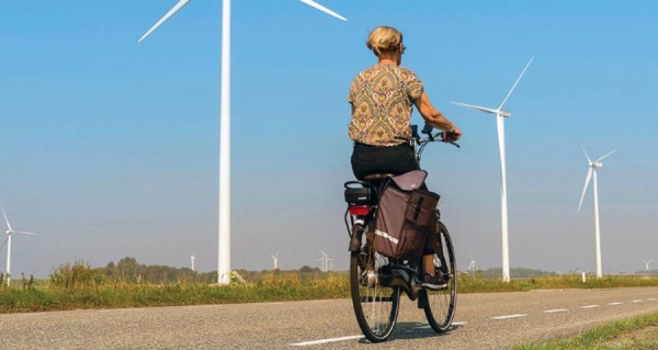 A woman cycles past wind turbines on a country road in Heijningen, The Netherlands. — courtesy Unsplash/Les Corpographes