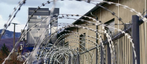 Barbed wire fencing surrounds a detention center. — courtesy Unsplash/Hédi Benyounes