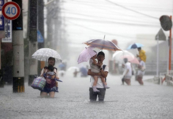 People walk on a flooded road in Kurume, Fukuoka Prefecture on Saturday. — courtesy Kyodo