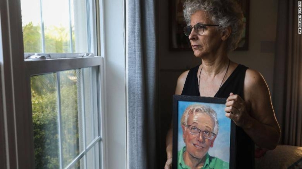 Cindy Johnson holds a painting of her husband, Steven, a retired pharmacist who had survived colon cancer but died of Covid-19, which Cindy believes he contracted at Blake Medical Center in Bradenton, Florida, where he was admitted for an infection in his hip.