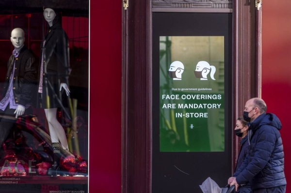 People walk past a sign requiring people to wear face coverings in London. (Xinhua)